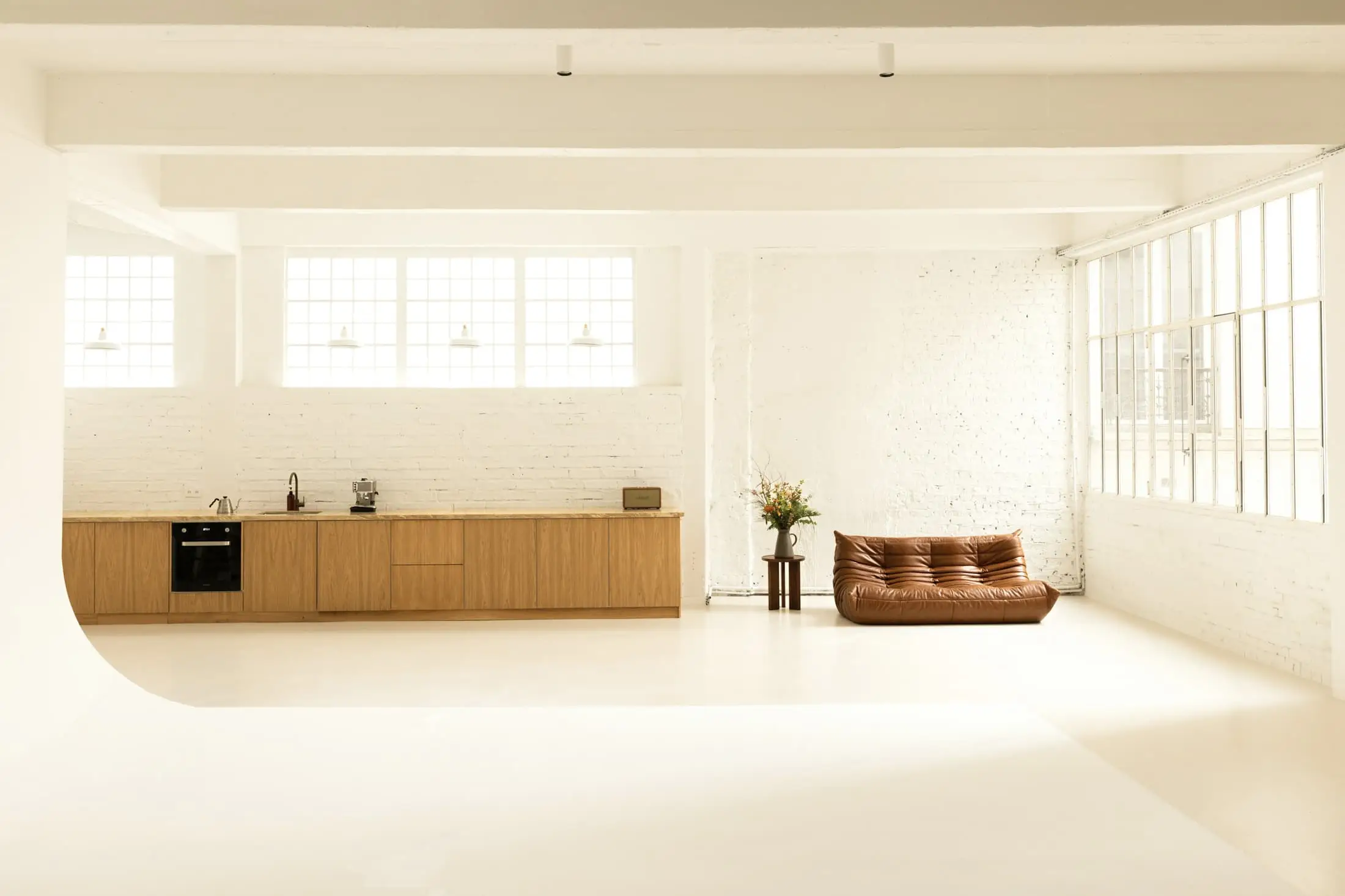 A wide cream room with an oak kitchen, a low sofa and steel-framed windows.
