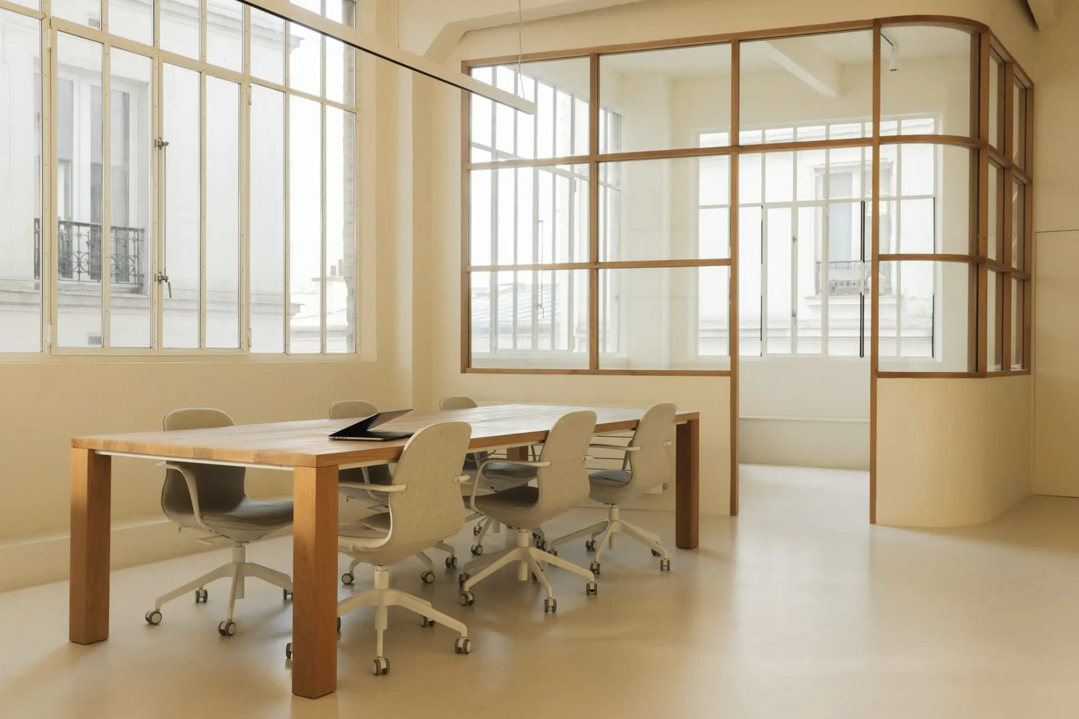 An oak meeting table and chairs behind a slender oak-framed glass screen in a cream room.