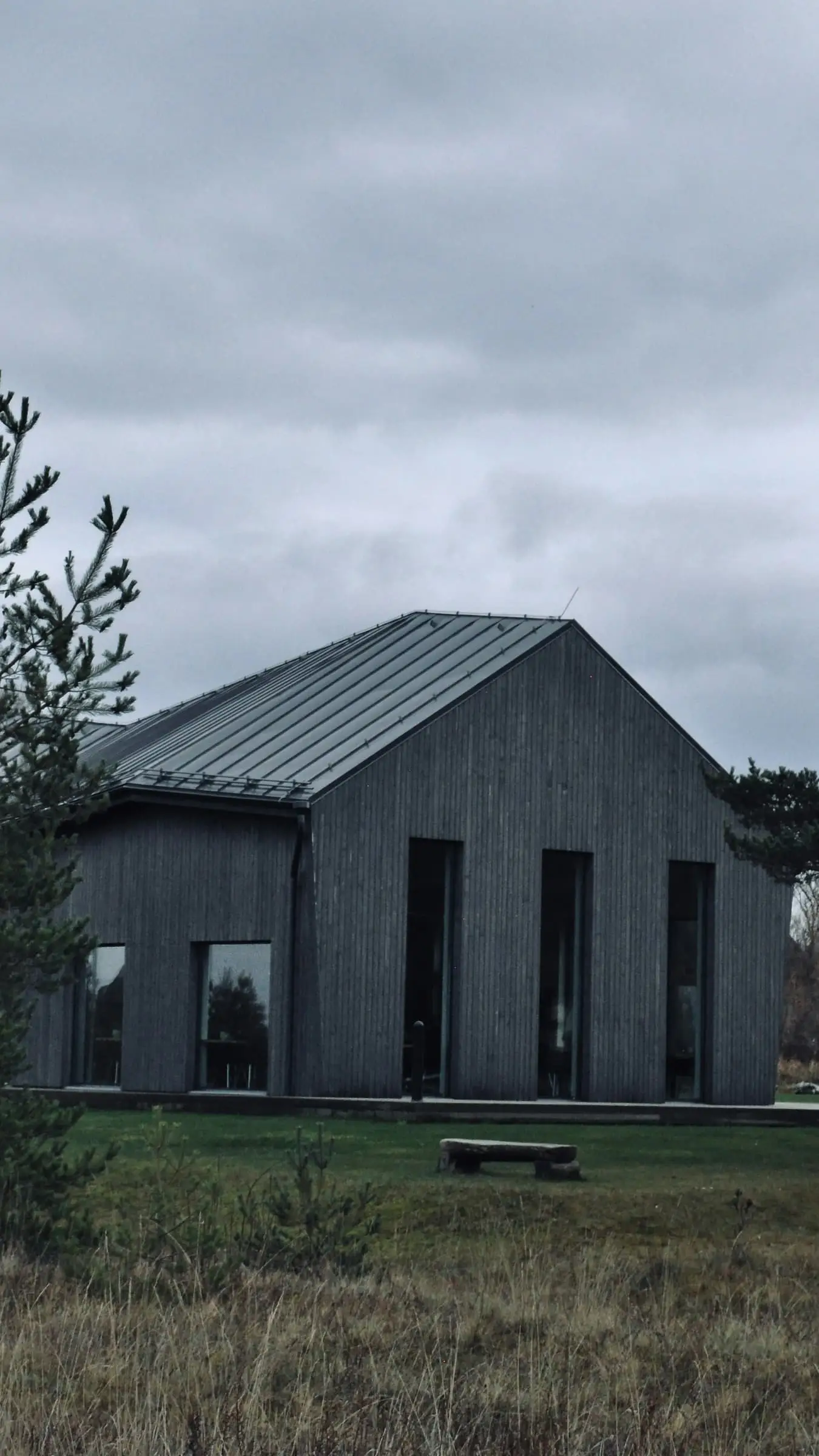A plain grey timber shed under a heavy sky, with long grass in front.