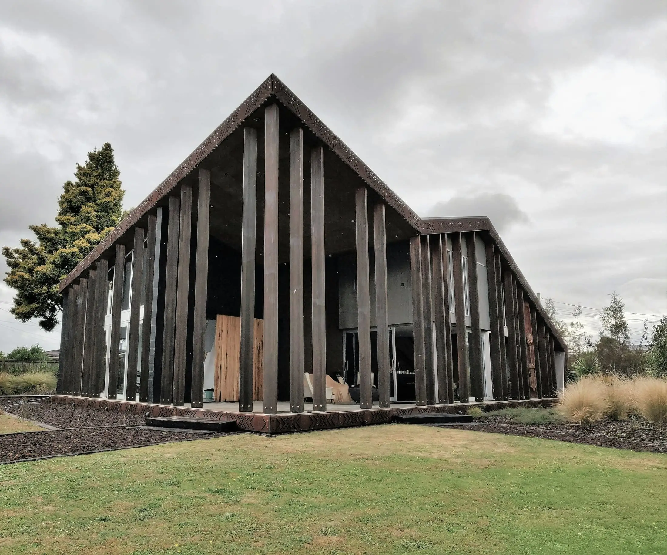 A tall black timber-finned gabled building on a green field.