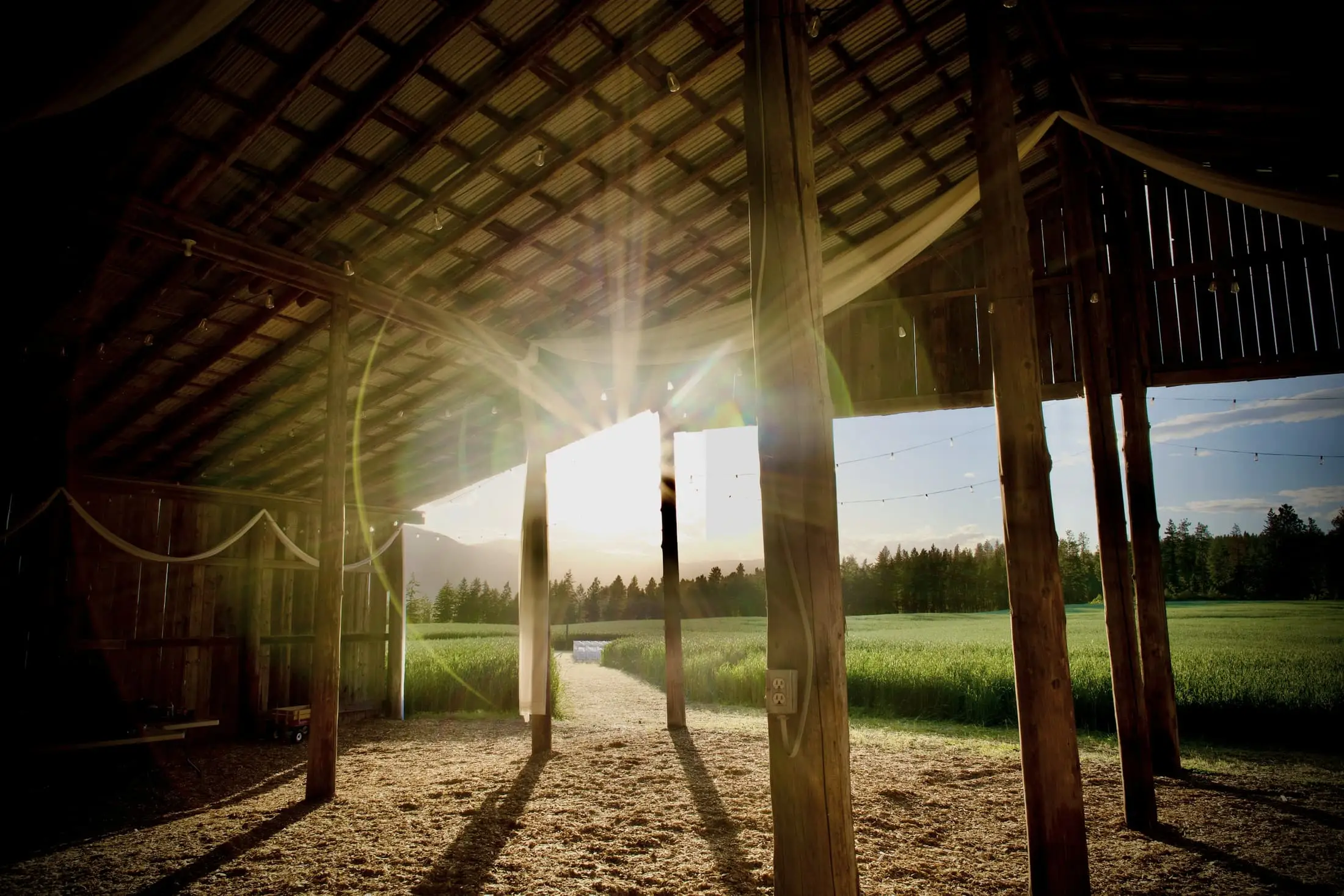Low sunlight through the open side of an old timber barn, with fields beyond.