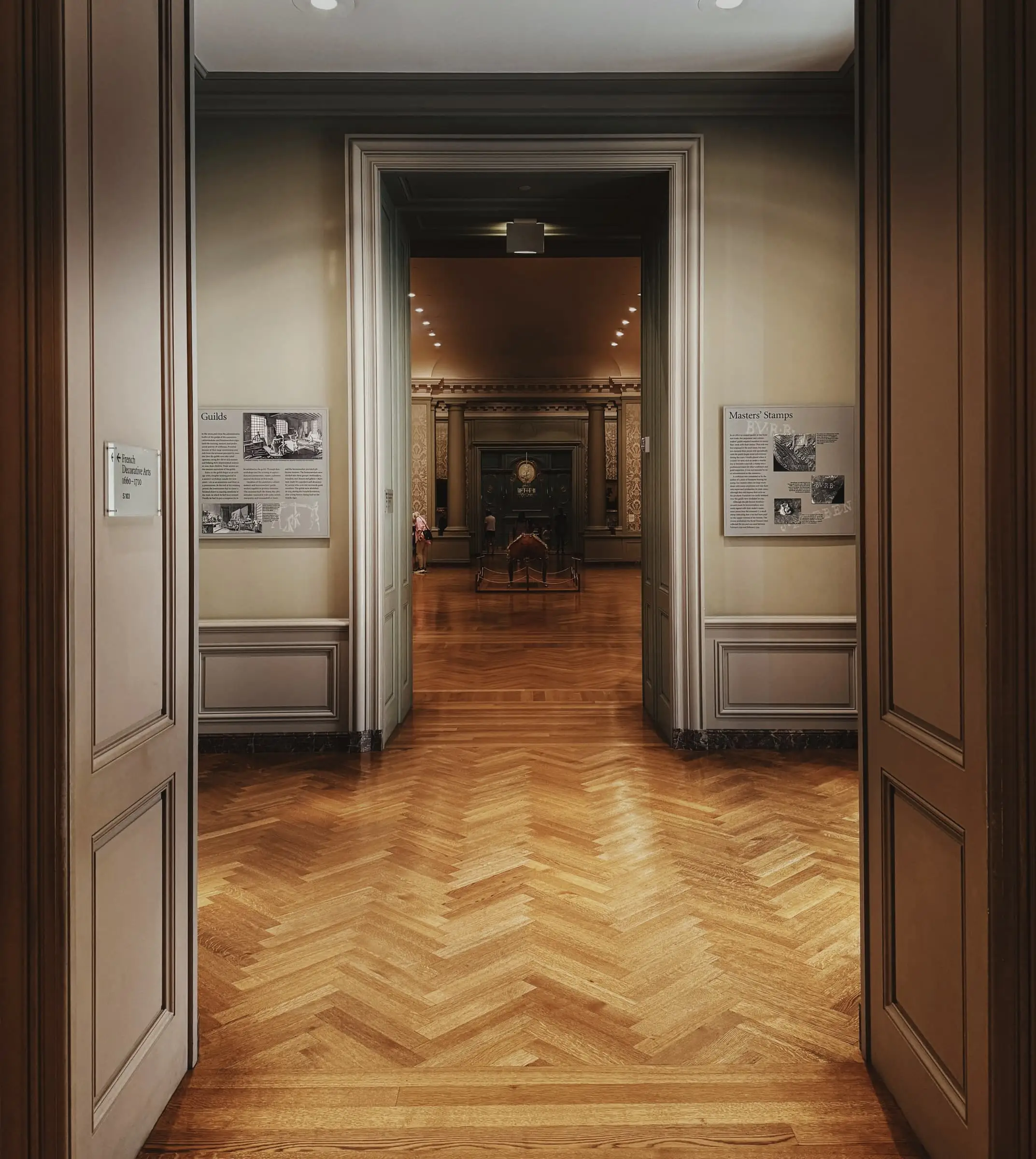 A view through a pair of tall doors along a line of rooms with herringbone parquet.