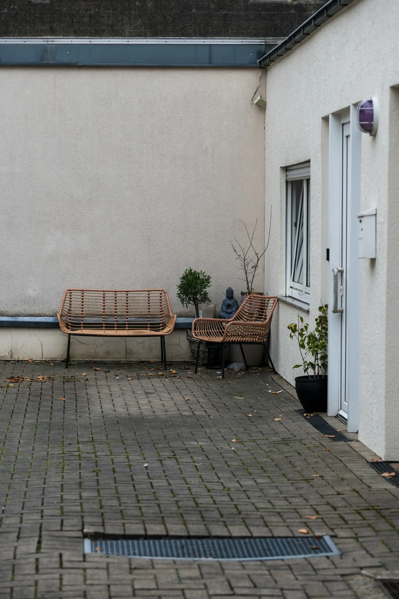 A white-walled courtyard with brick paving, a wooden bench and a long grate.
