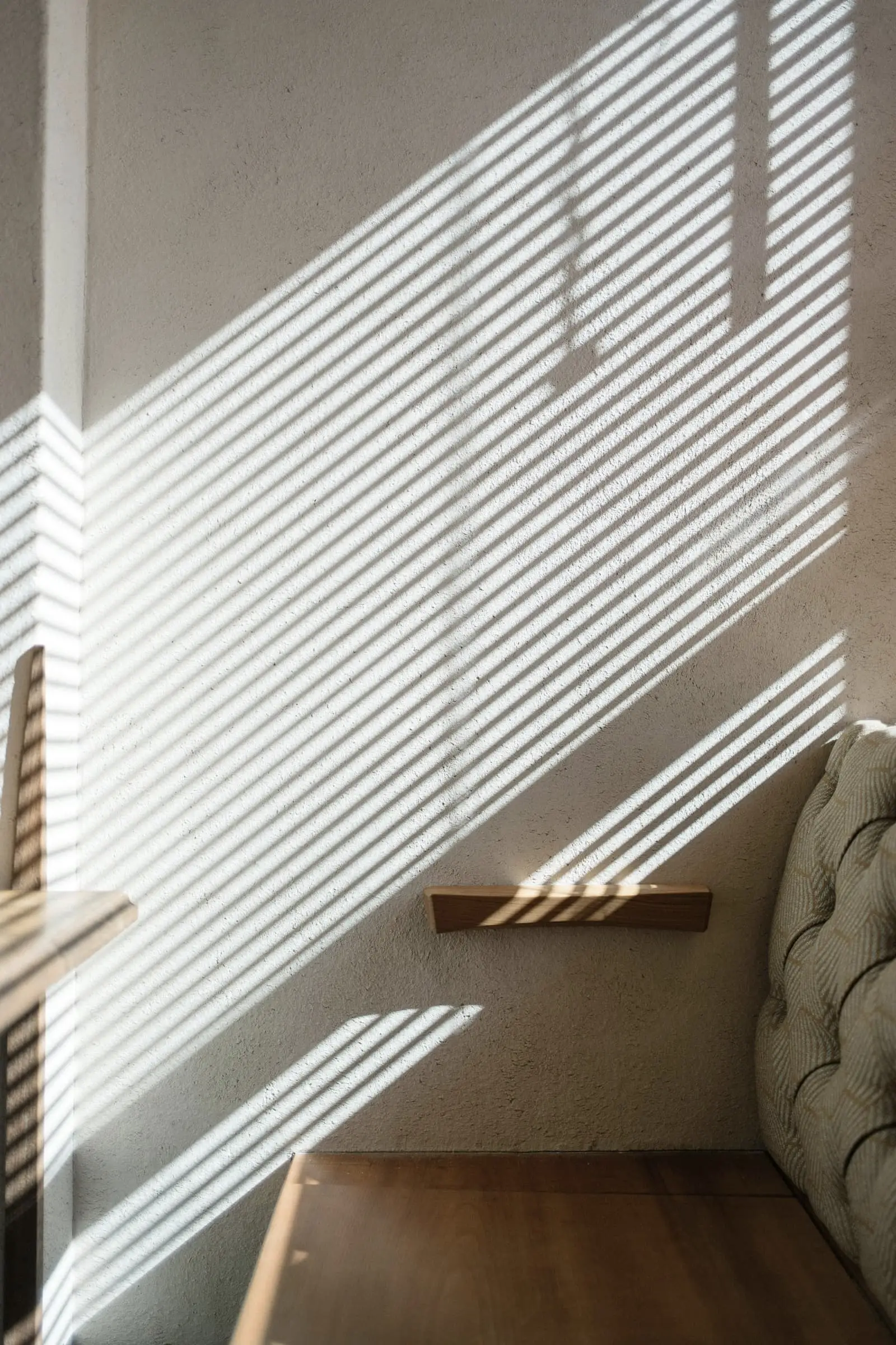 A white stair hall with bands of sunlight through a slatted screen and an oak shelf.