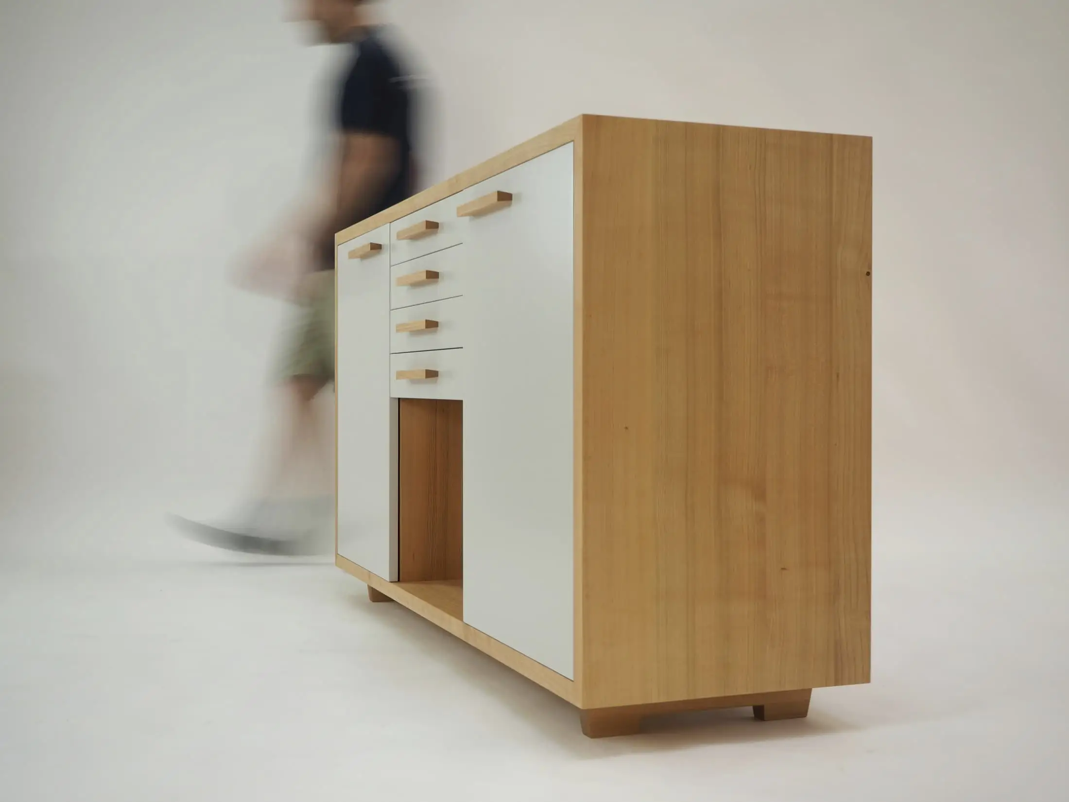 A person walking past a freestanding oak and white cabinet against a white backdrop.