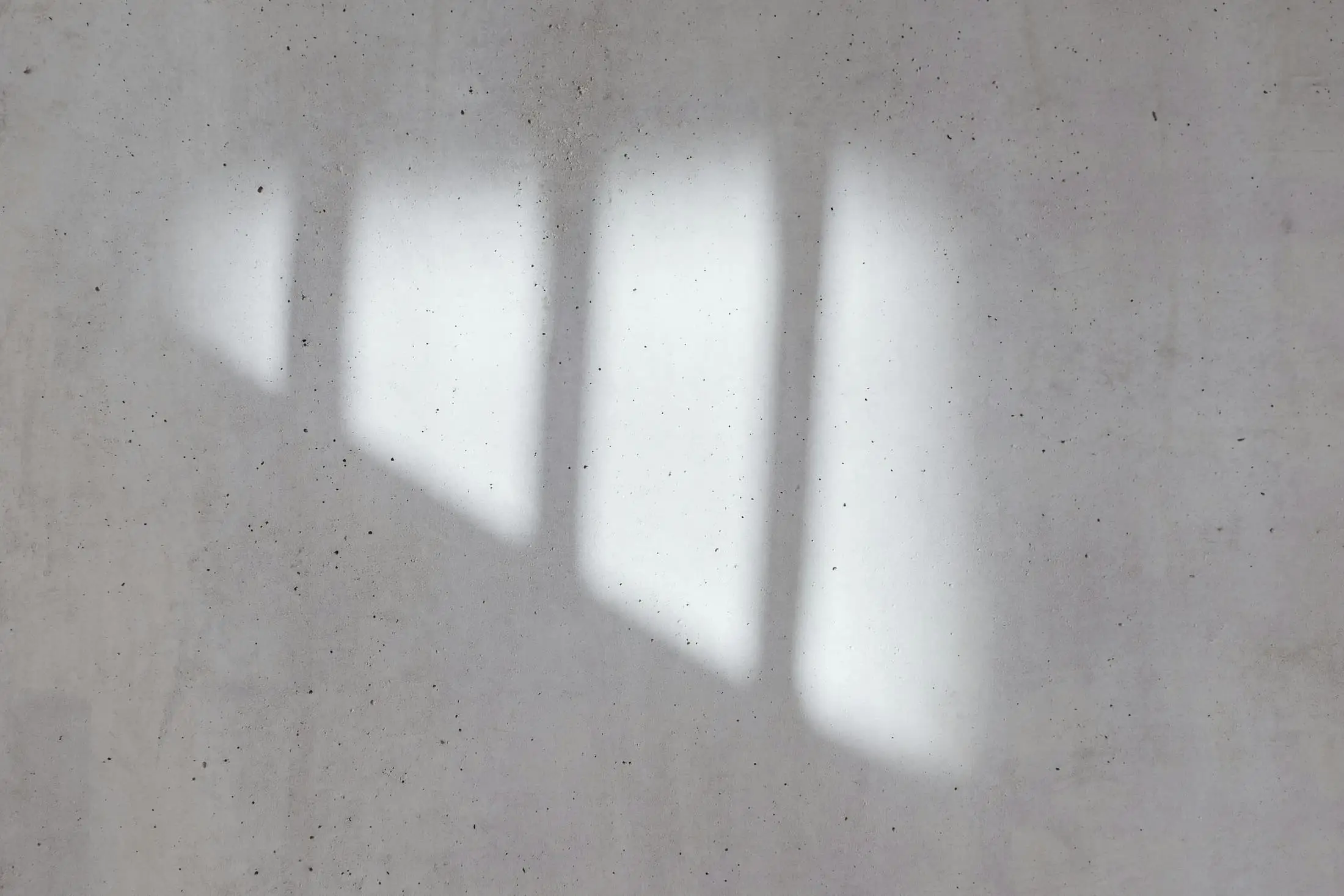 The shadow of a window frame cast across a grey plaster wall.