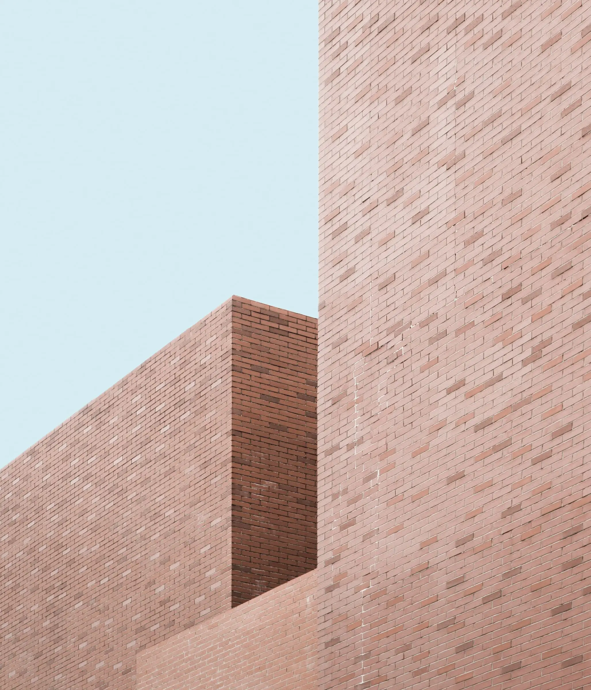 Two stepped volumes of pale red long-format brick against a clear sky.
