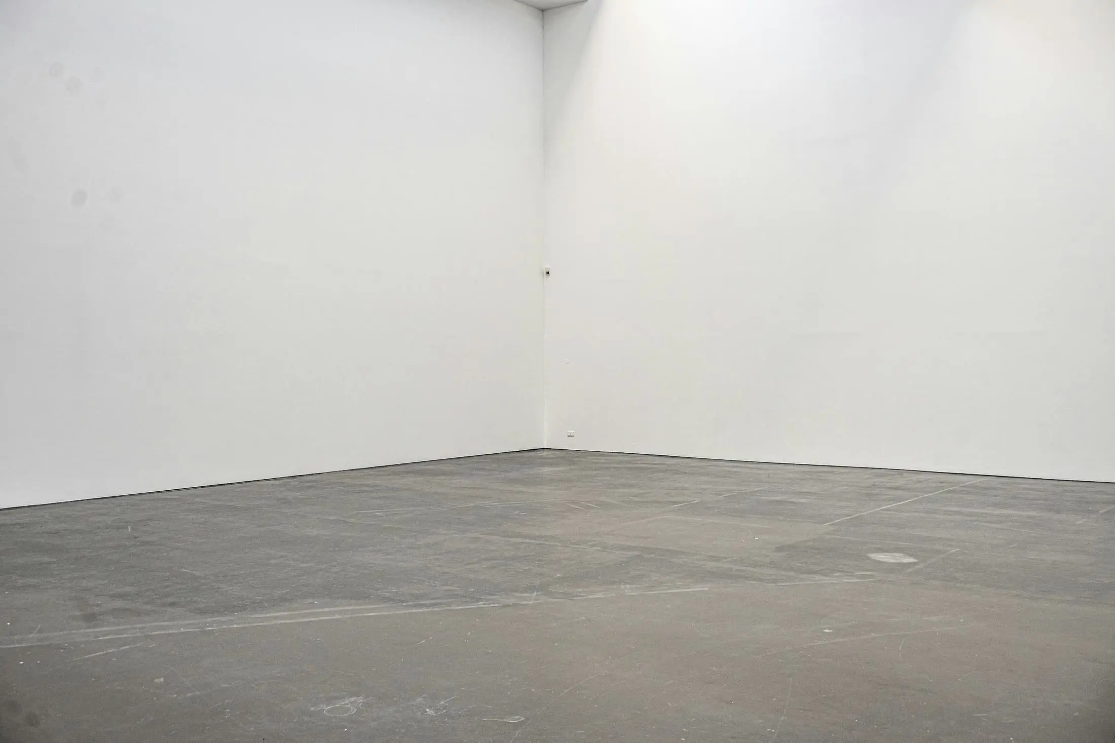 The corner of an empty room where white walls meet a grey concrete floor.