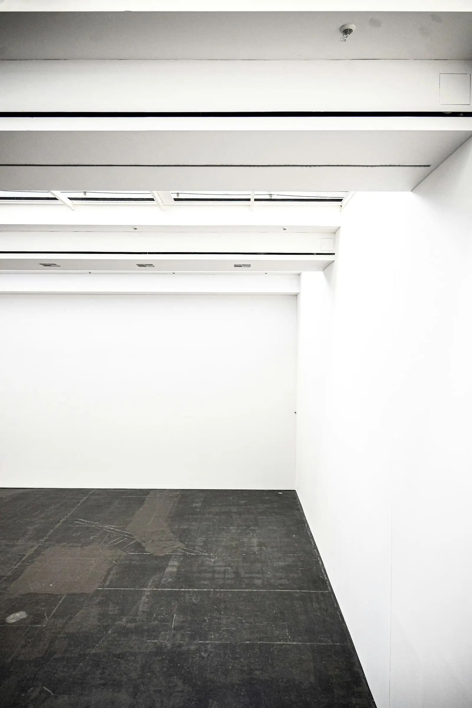 A white room with a dark floor and bright ceiling light, seen through an opening.