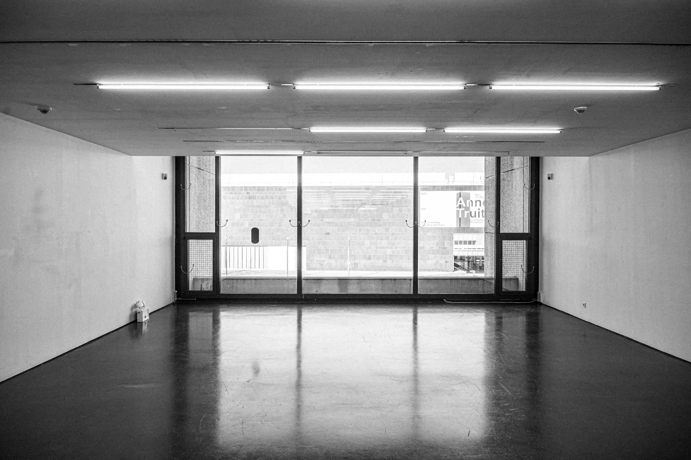 The end wall of a long gallery with large windows and rows of fluorescent lights.