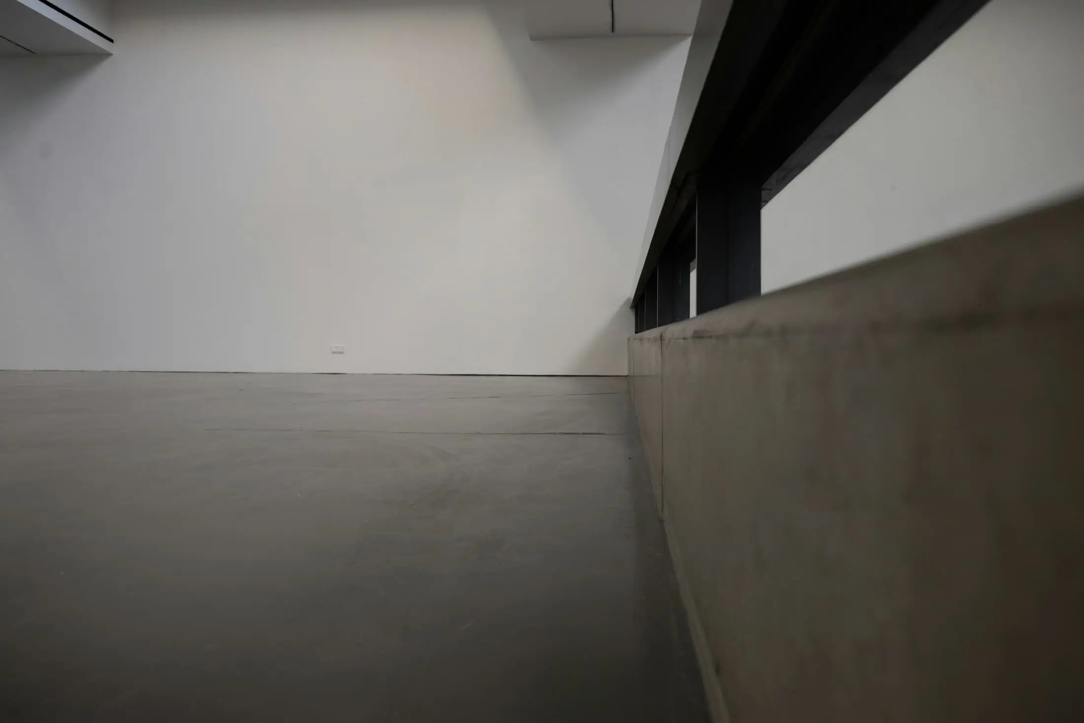 A concrete upstand along a dim empty room with a white wall.