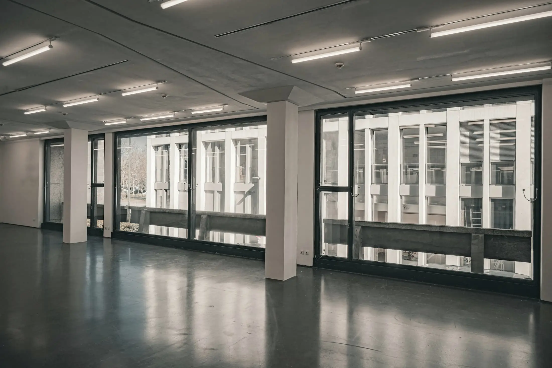 A wide empty hall with reflective floor and ranks of large steel-framed windows.