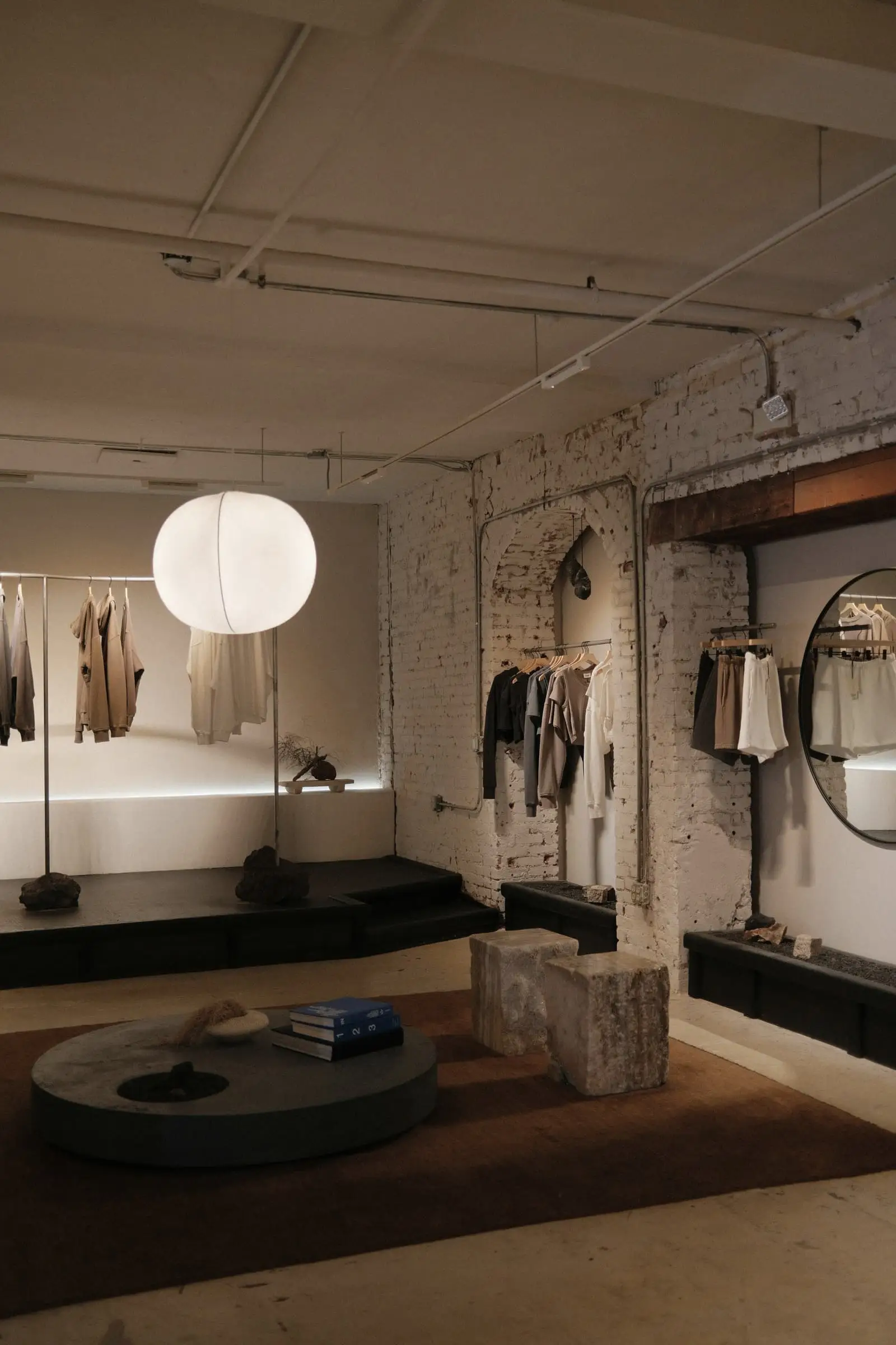 A dim room with a paper pendant, a low shelf and a clothes rail with objects on display.