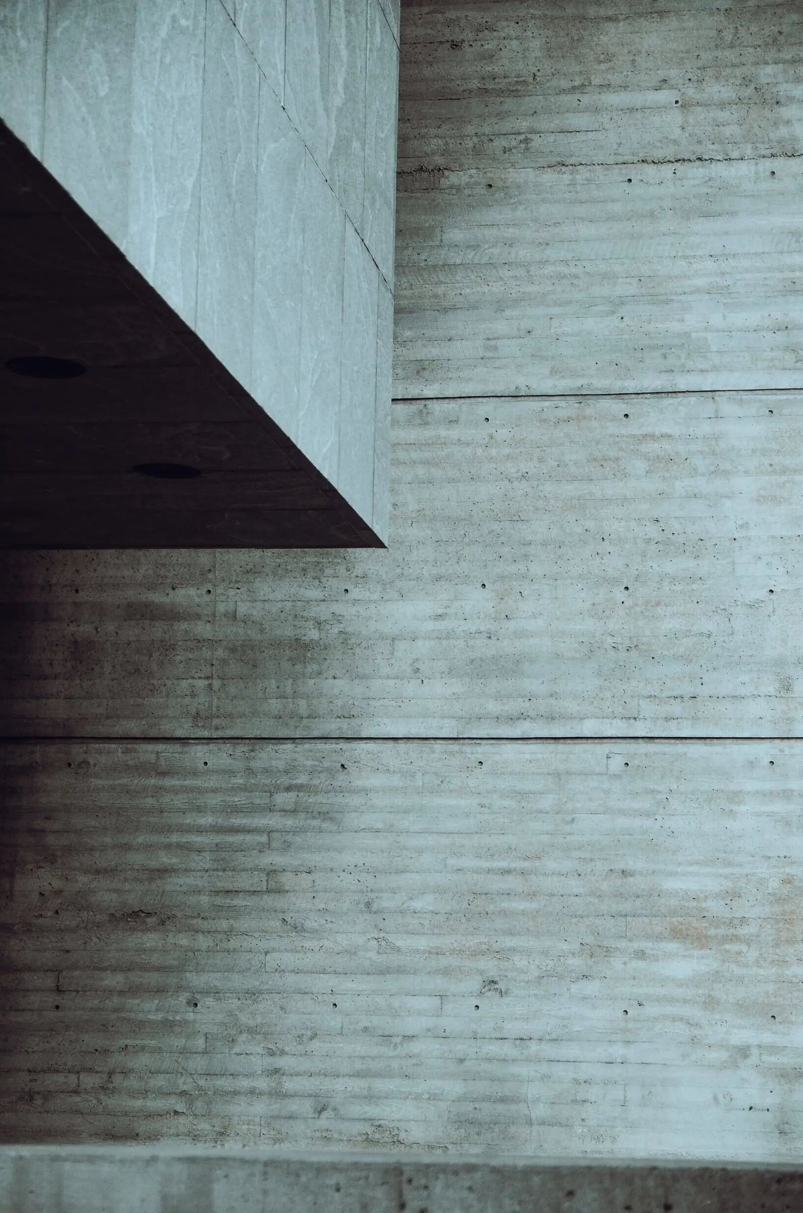 A board-marked concrete wall in shade with a sharp diagonal shadow.