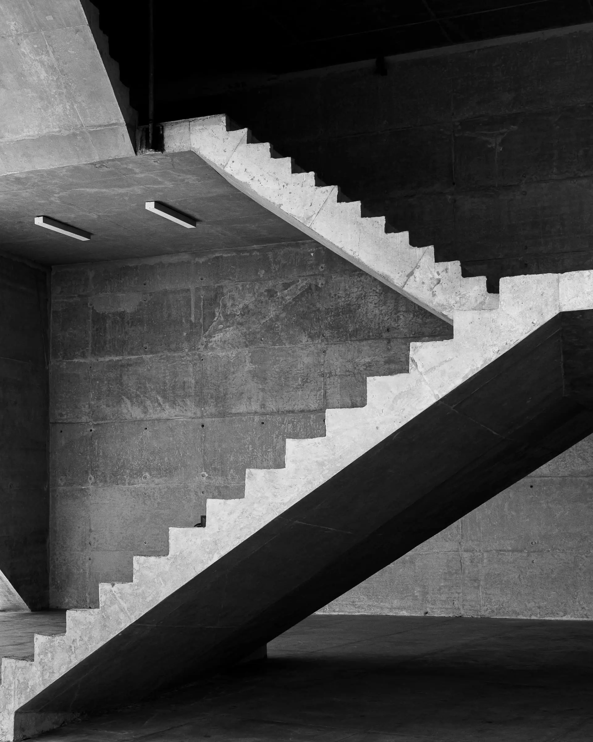 A concrete staircase in grey light with a strip of daylight above it.