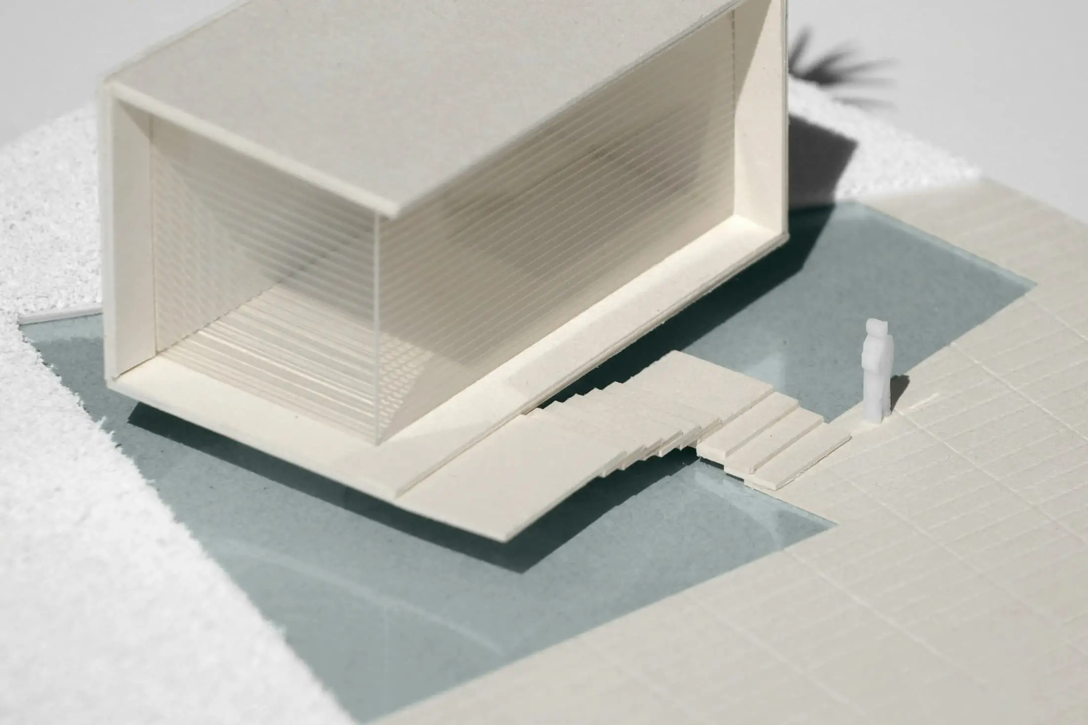 A pale card model showing a tilted roof, a long stair and pale green water.