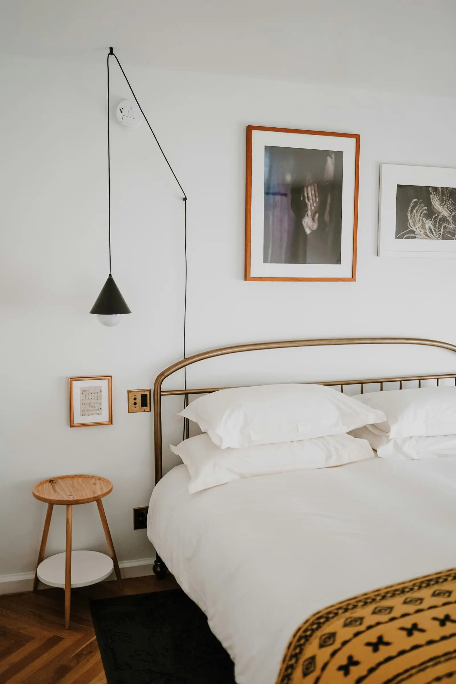 A white bed with an iron frame, a stool and framed pictures on a white wall.