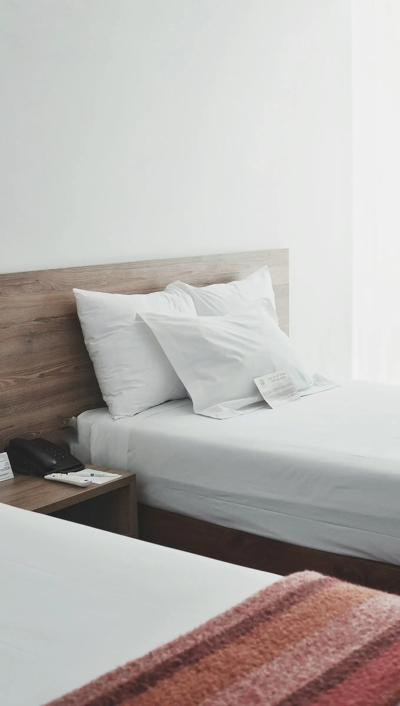 A white bed with a timber headboard in a bright room.