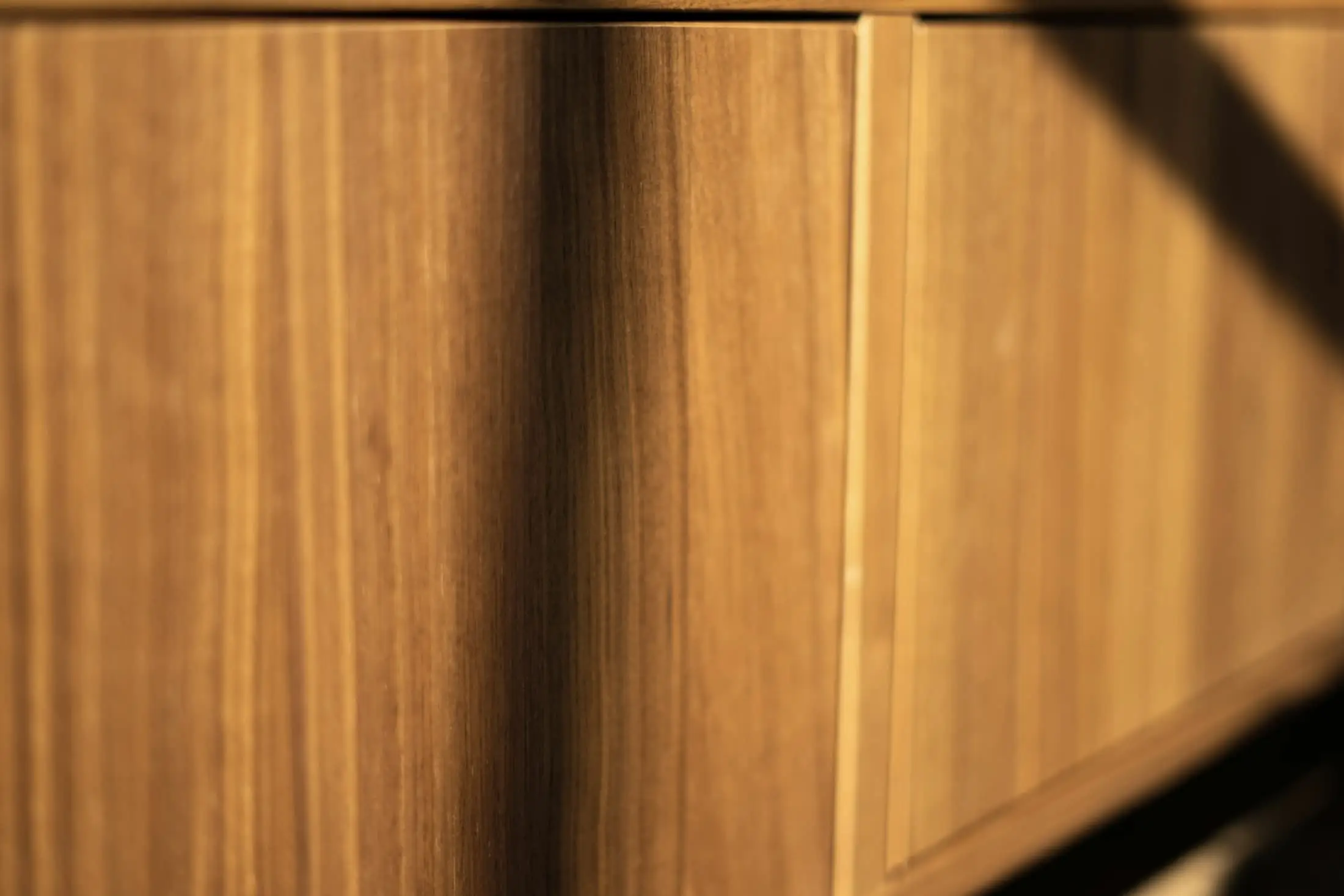 Warm oak cabinet panels crossed by a band of shadow.