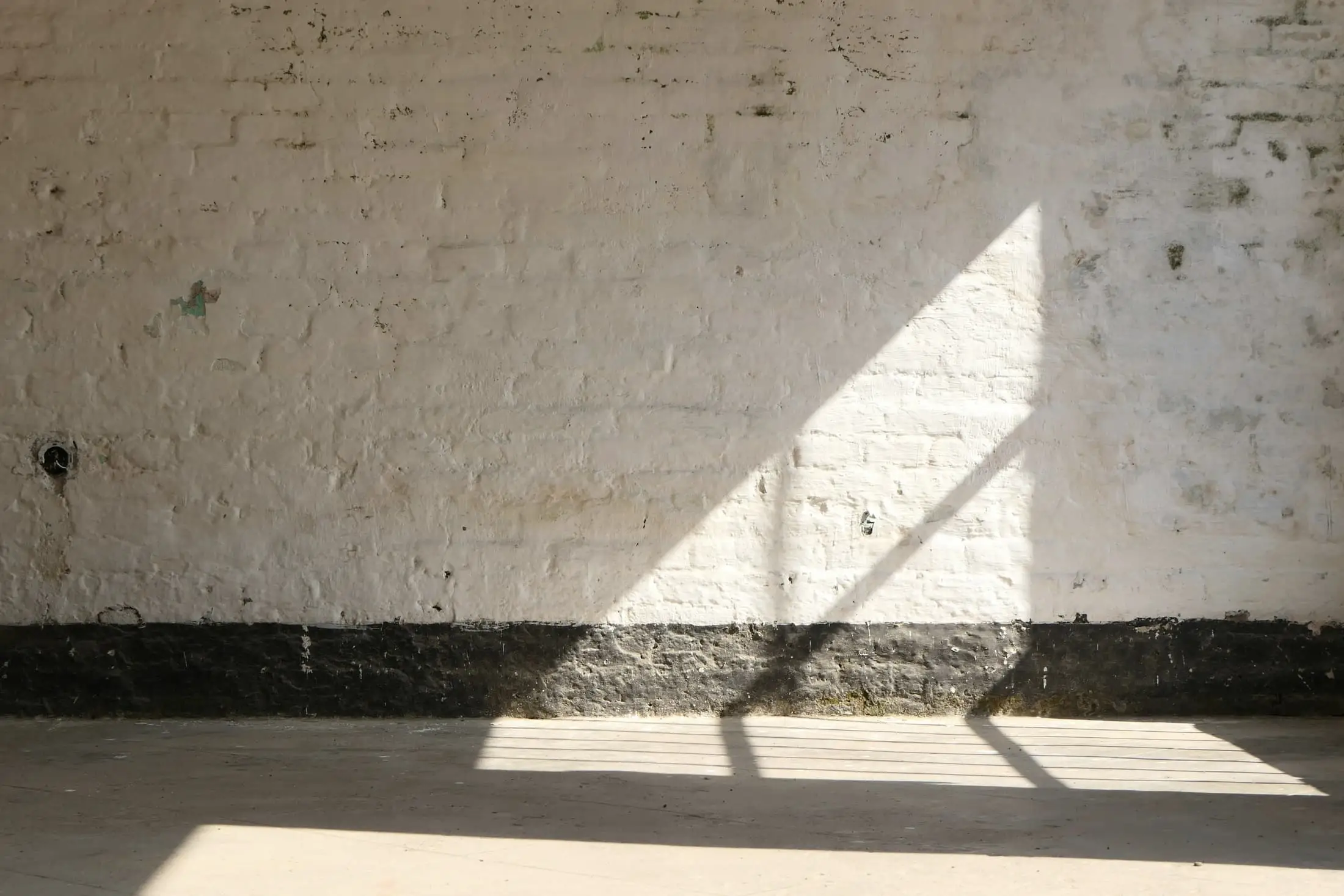 A whitewashed brick wall lit by a low band of sunlight on the floor.