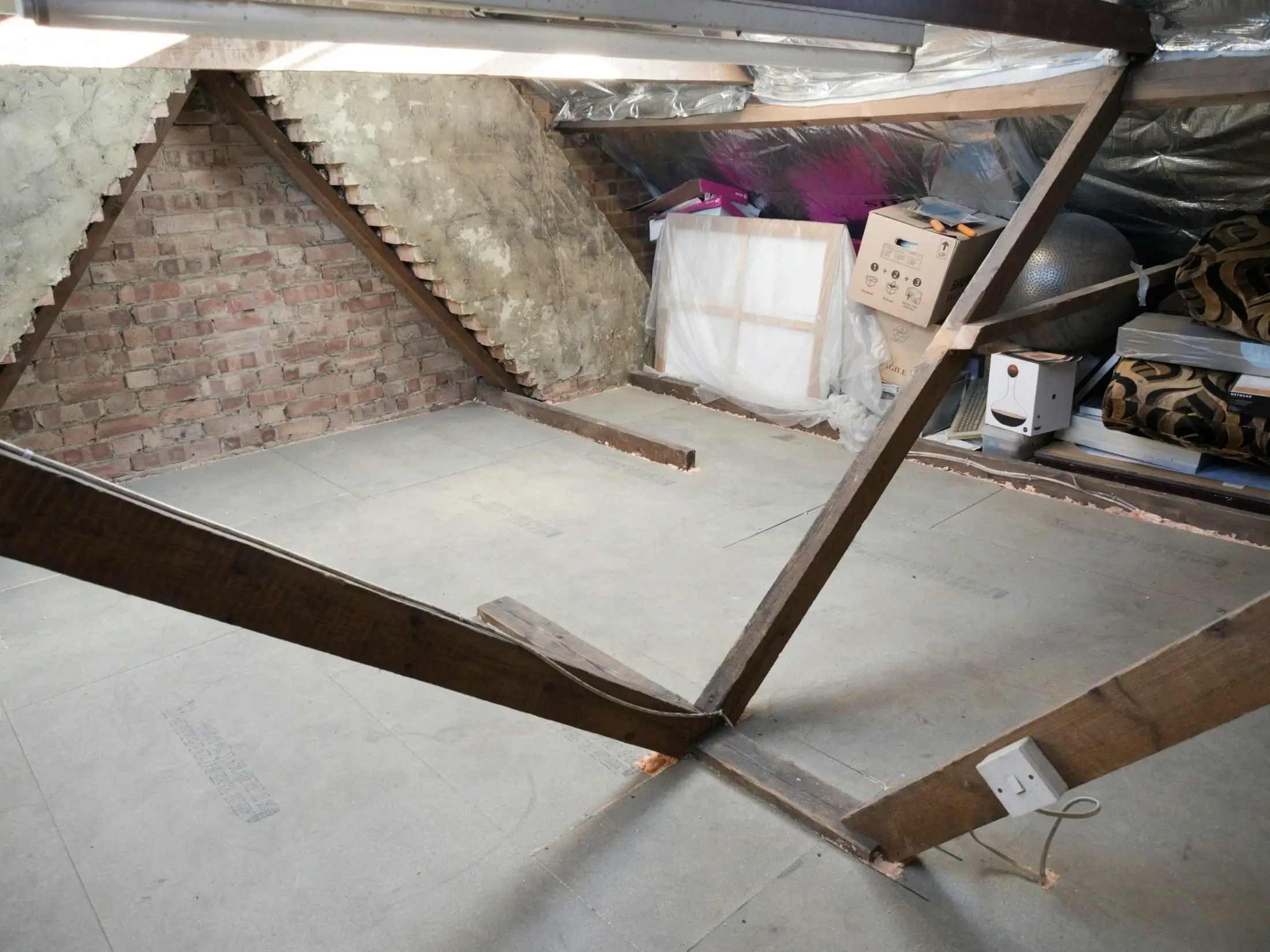 A dusty attic with diagonal timber beams and insulation boards.
