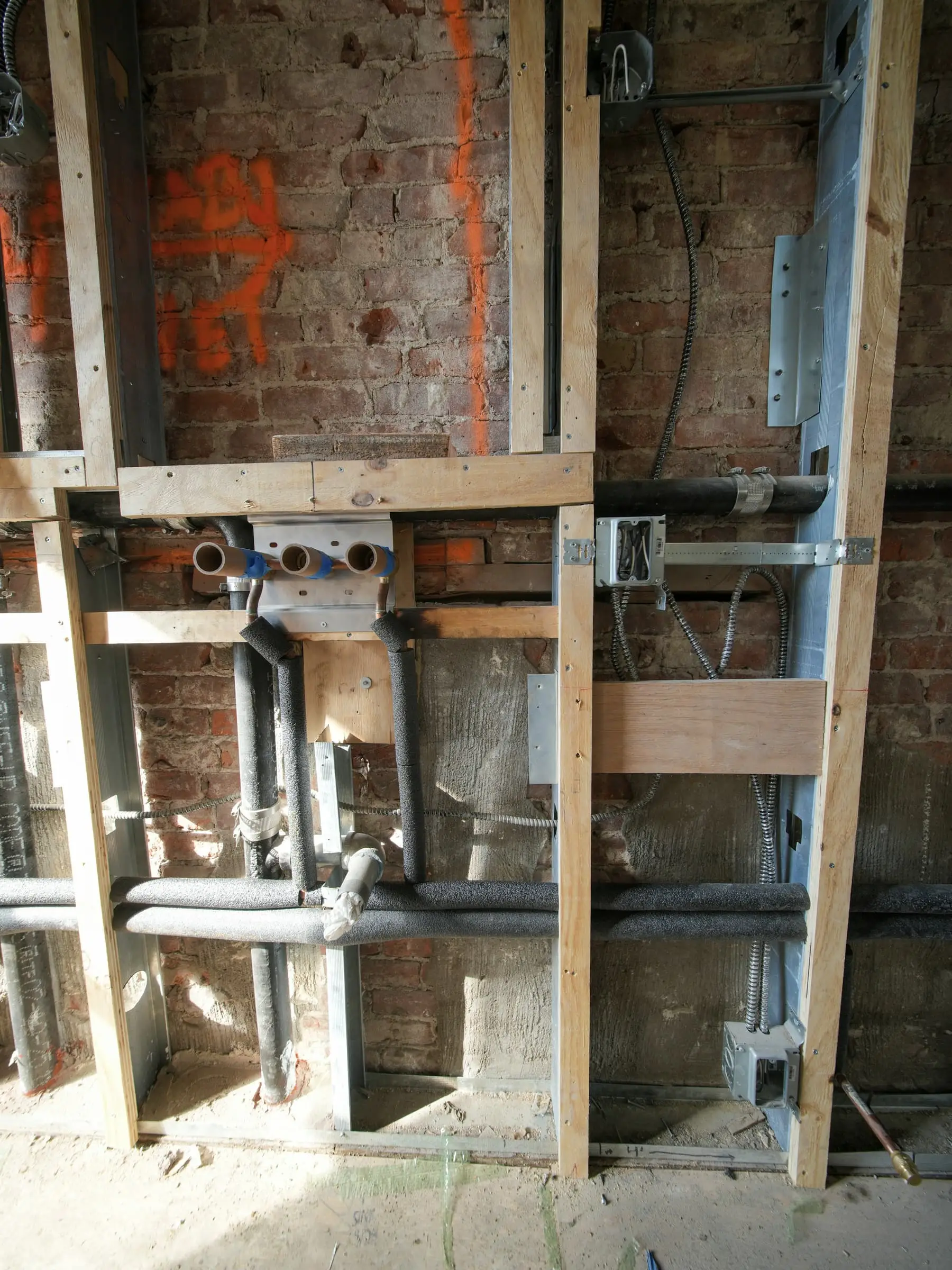 Exposed brick, new pipes and wiring and timber framing within a wall under renovation.