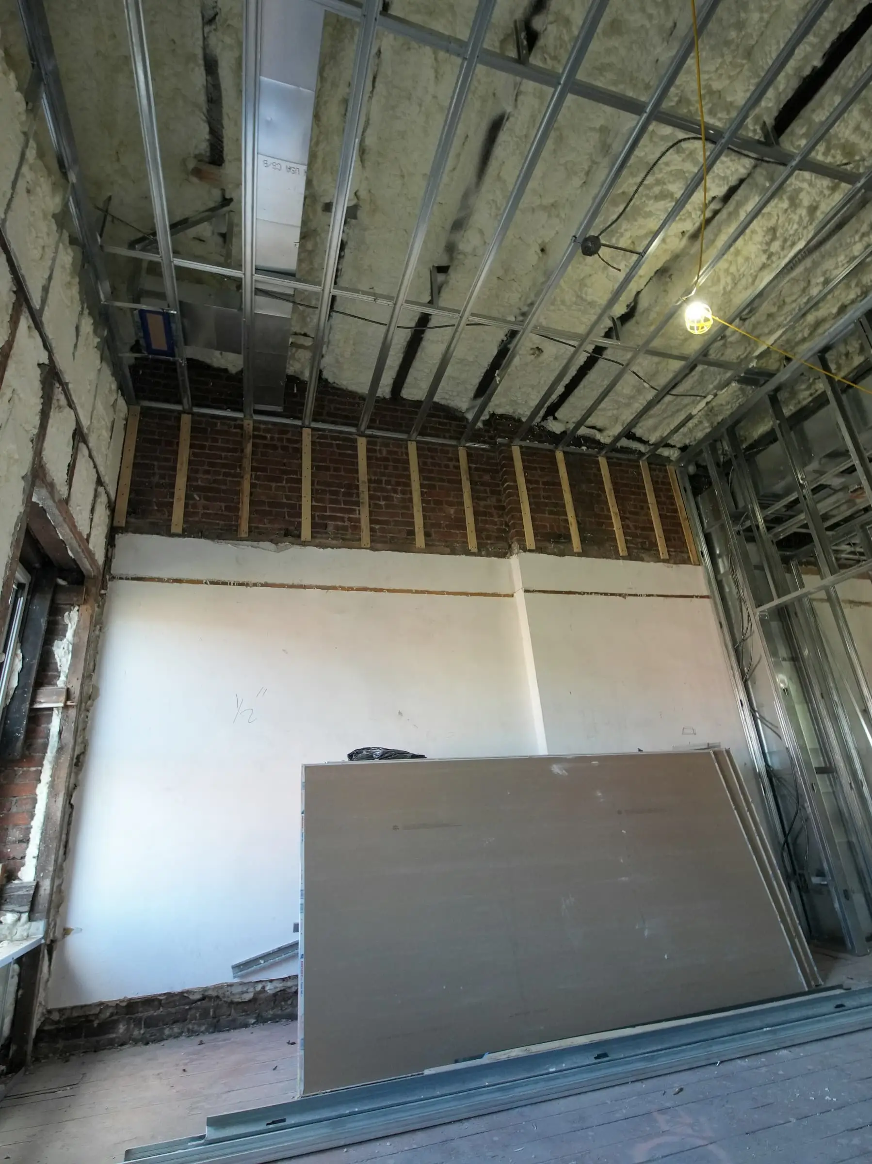 A room under construction, with metal studs, exposed ceiling and leaning plasterboard.