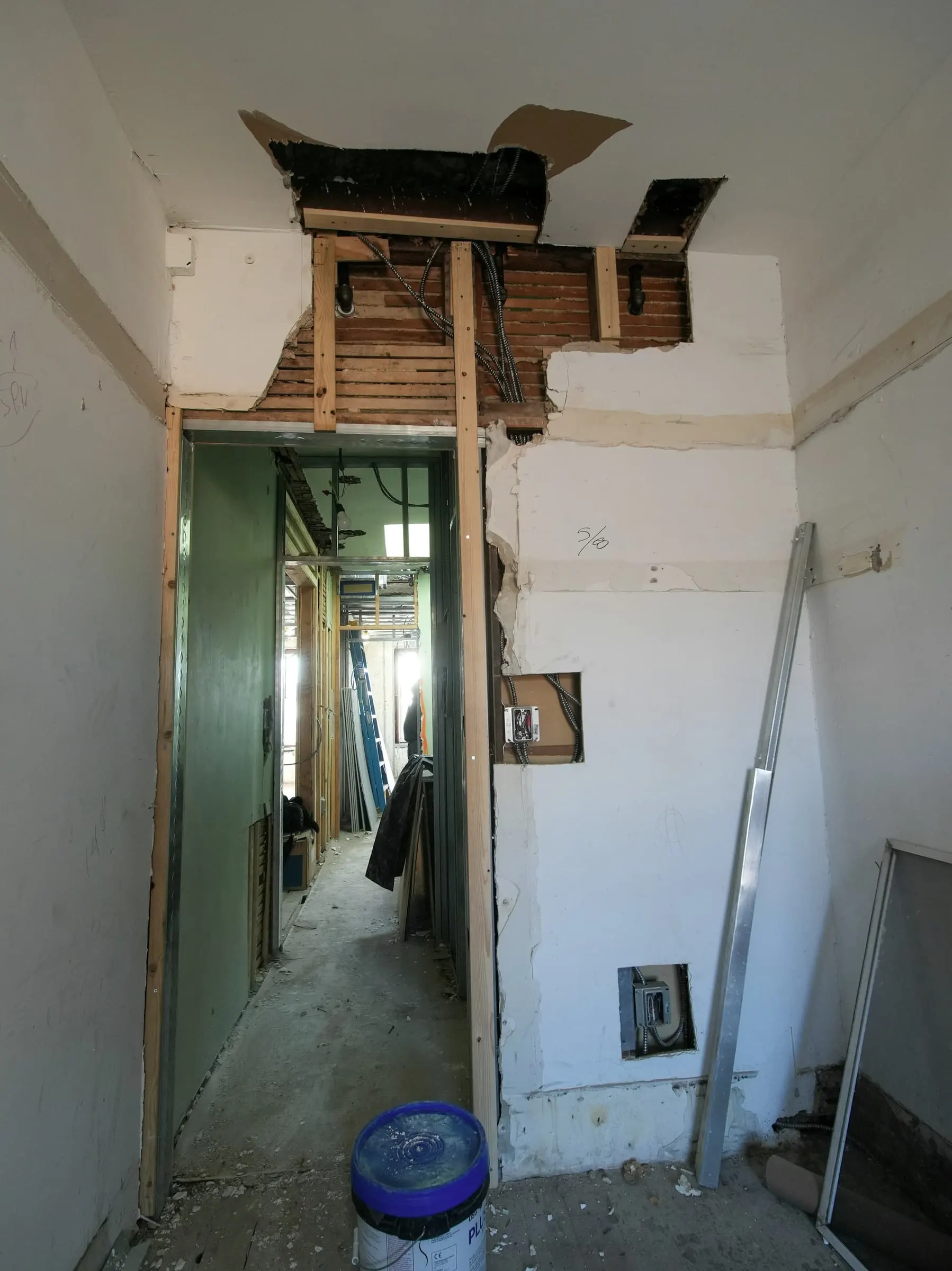 A narrow room mid-renovation with broken-out walls and an opening through to the next room.