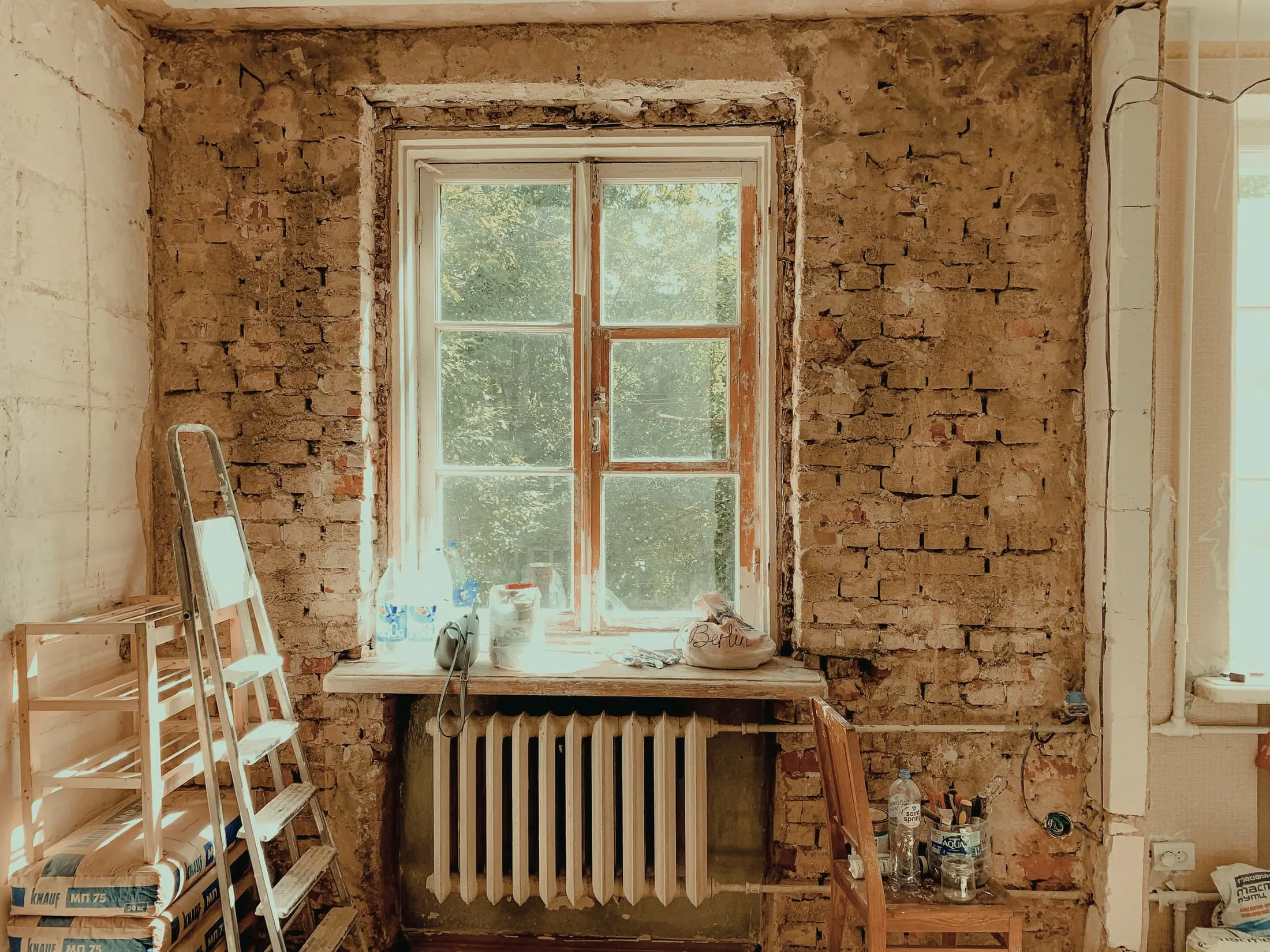 A stripped room with bare orange brick around a window and a radiator beneath it.
