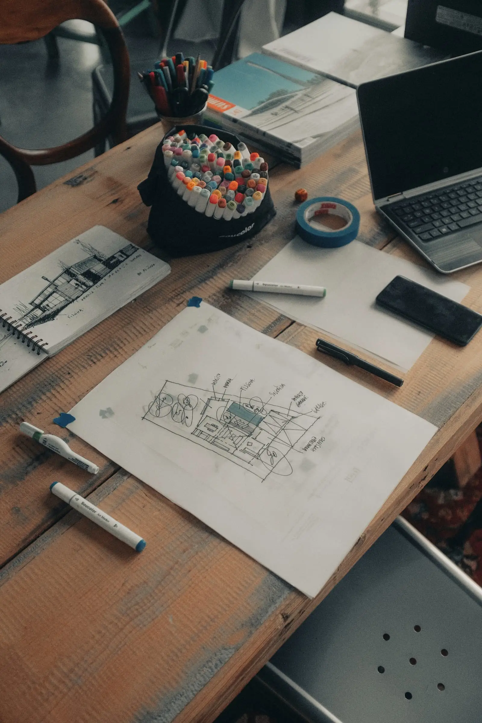 A drawing of a floor plan on a timber desk beside a calculator and laptop.
