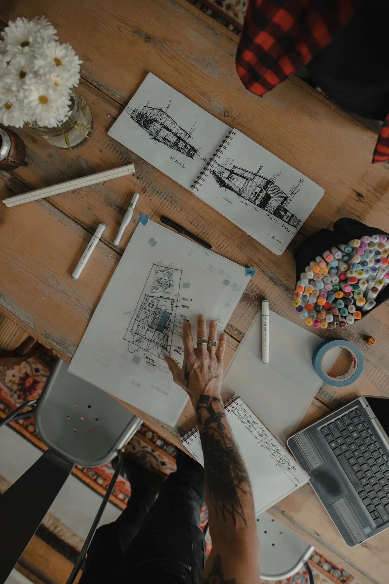 Hands sketching a plan on paper on a timber desk, seen from above.