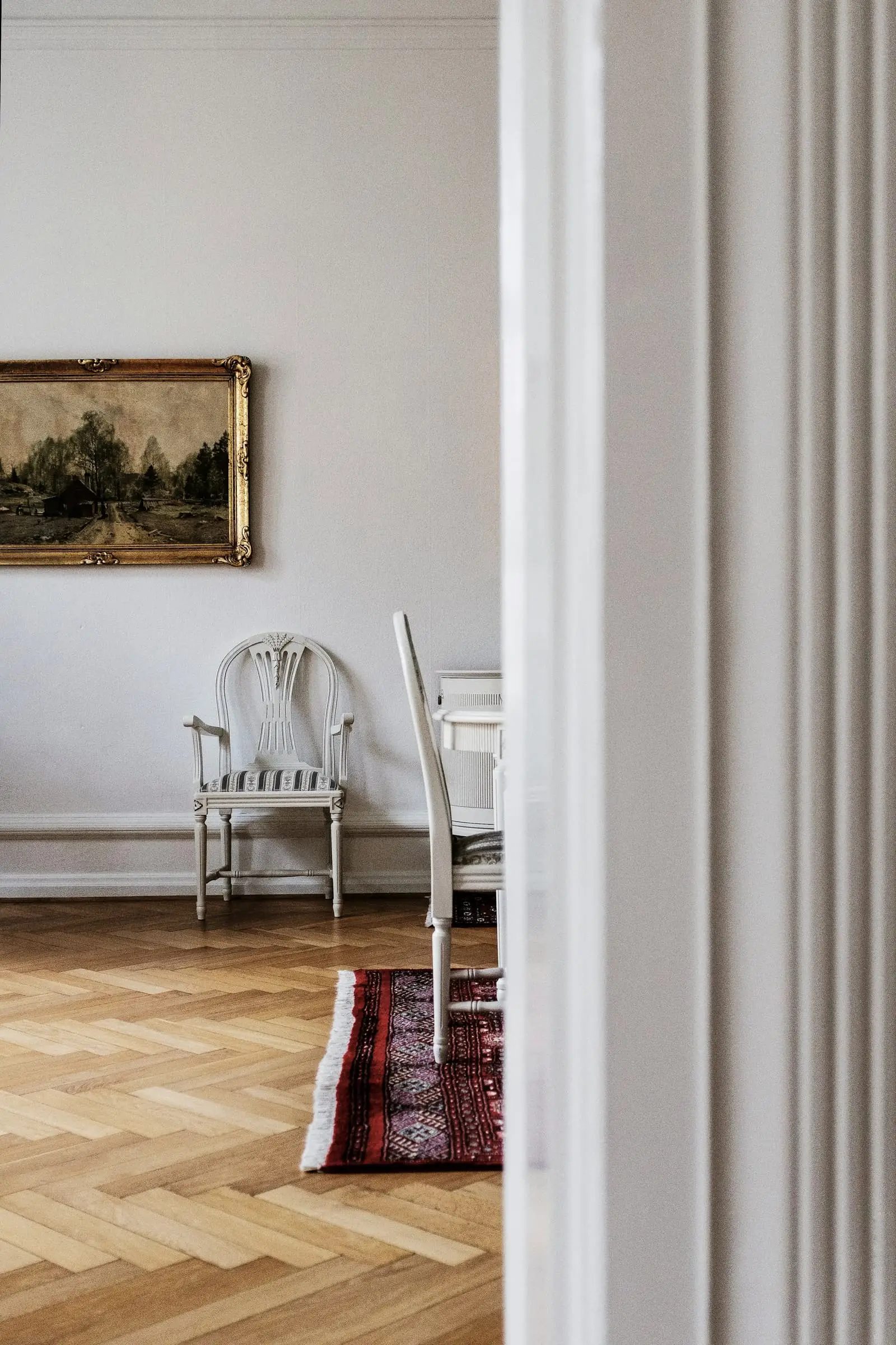 A white-panelled room with a parquet floor, a small rug and an armchair.