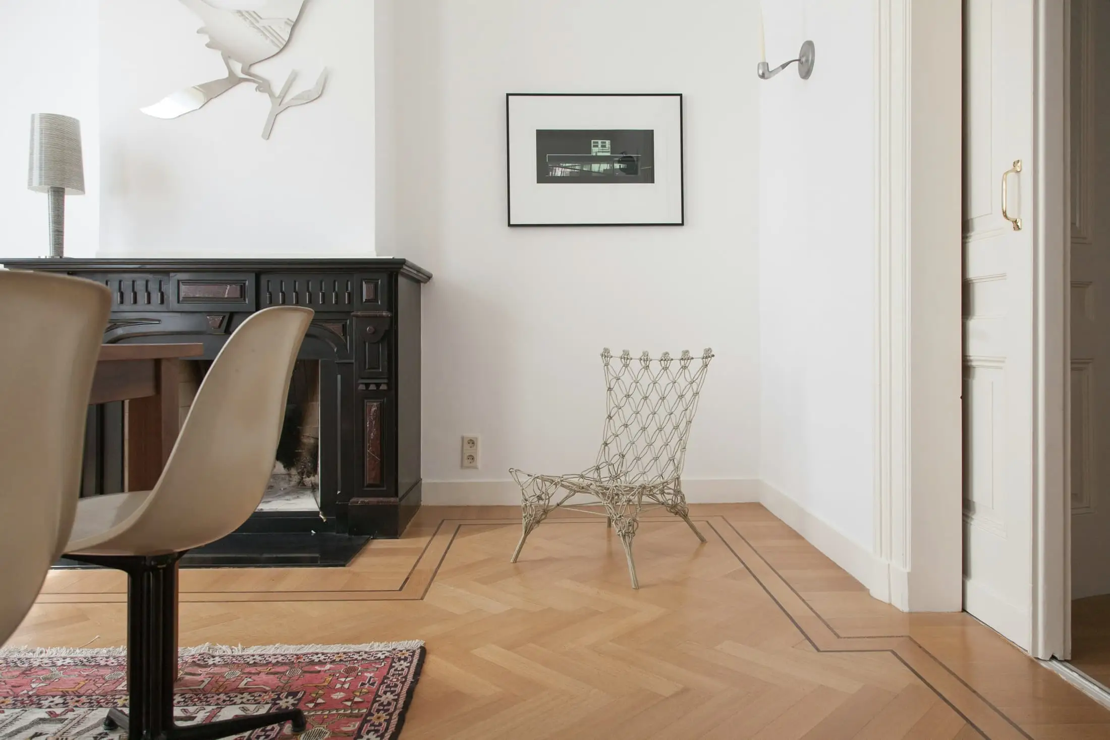 A white room with an oak floor, a dark chair and a framed picture.