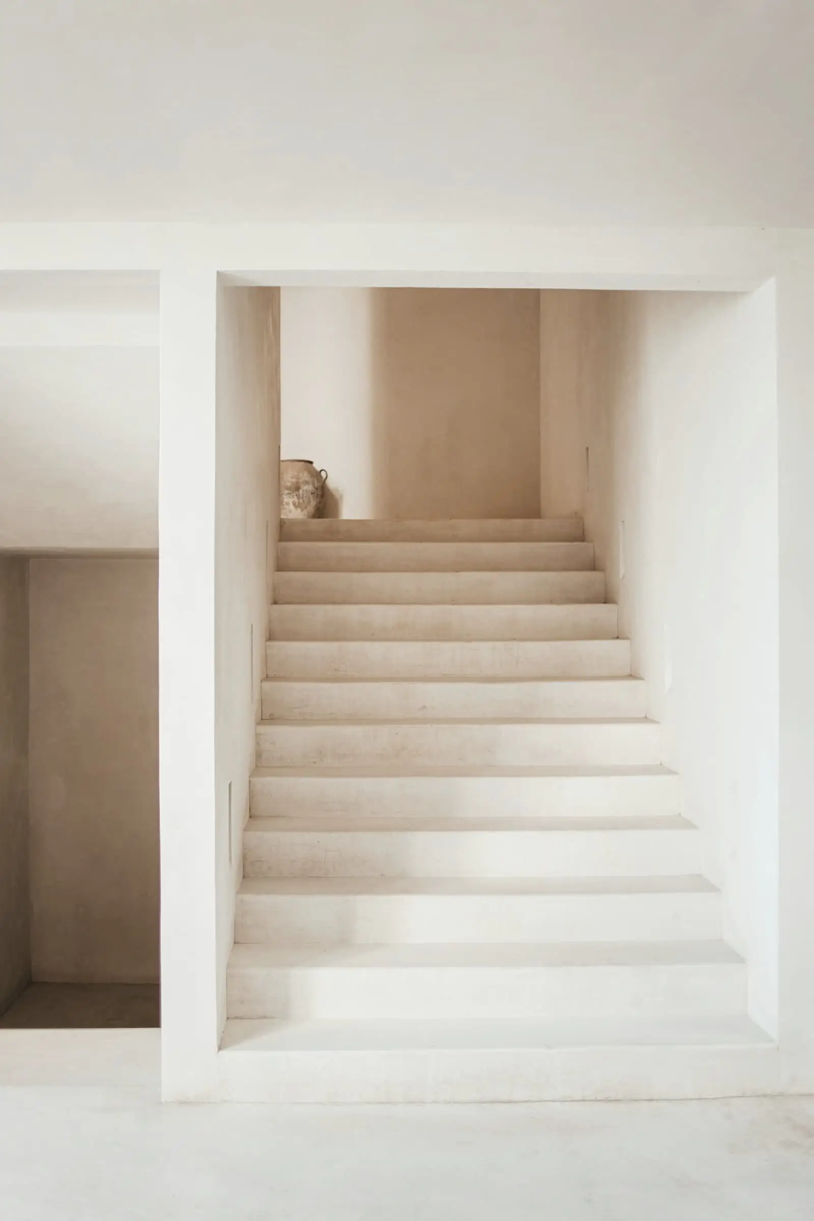 A pale plastered stair rising through a square opening, in soft light.
