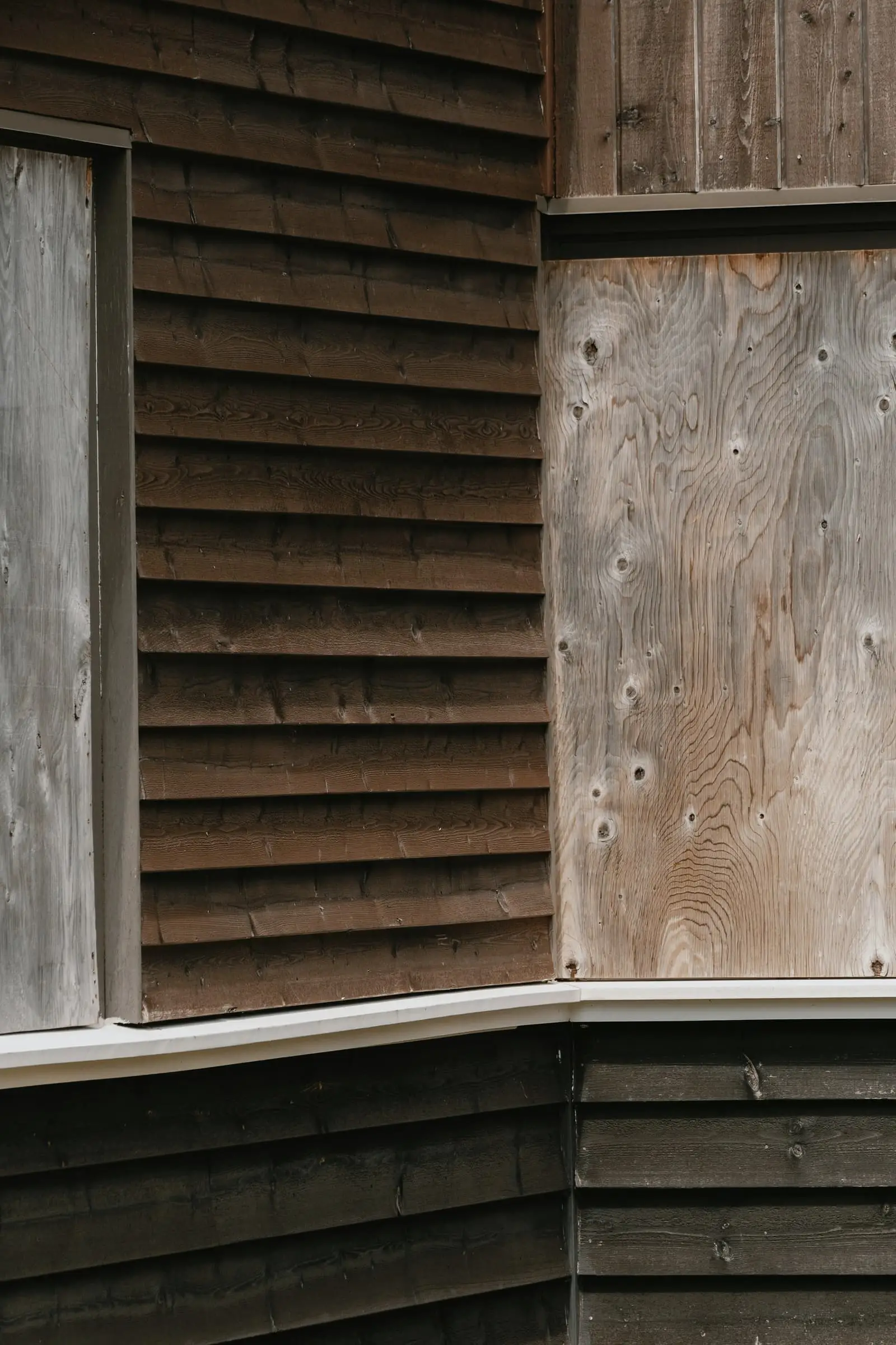 A corner of weathered dark timber boards meeting a pale panel.