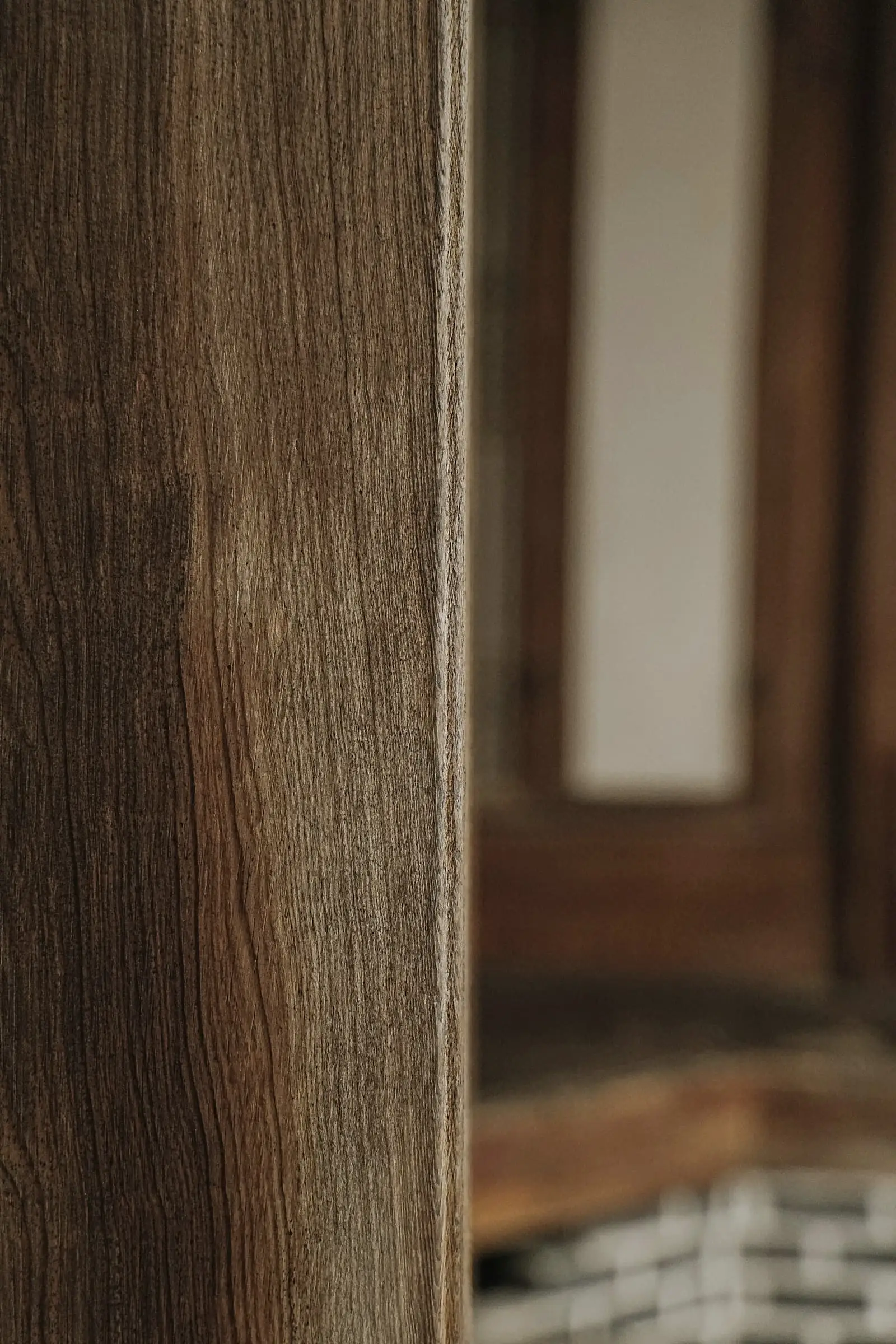 A close view of an oak post with a blurred doorway beyond.